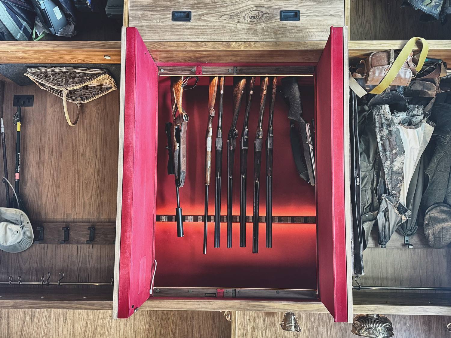 Concealed gun storage built into walnut joinery, opened to show baize-lined racking